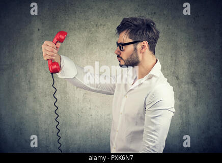 Seitenansicht des formalen Mann in Gläser holding Hörer vor Gesicht im Unverständnis auf grauem Hintergrund Stockfoto