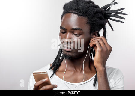 Afrikanischer Mann Kopfhörer tragen und halten sein Smartphone vor weißem Hintergrund Stockfoto