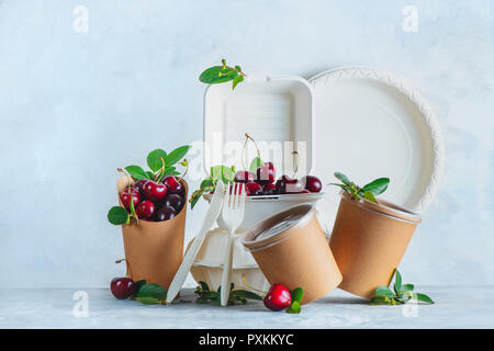 Gastronomie Einwegartikel, Tassen, Teller und Behälter mit Kirschen. Umweltfreundliche Verpackungen von Lebensmitteln auf einen neutralen grauen Hintergrund mit kopieren. Erhaltung Stockfoto