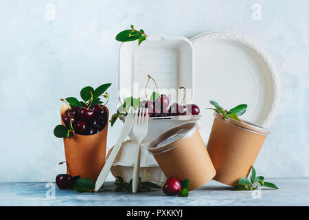 Gastronomie Einwegartikel, Tassen, Teller und Behälter mit Kirschen. Umweltfreundliche Verpackungen von Lebensmitteln auf einen neutralen grauen Hintergrund mit kopieren. Erhaltung Stockfoto