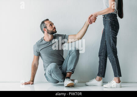 7/8 shot der jungen Frau die Hand, bärtiger Mann sitzen auf dem Boden zu depressiven Stockfoto