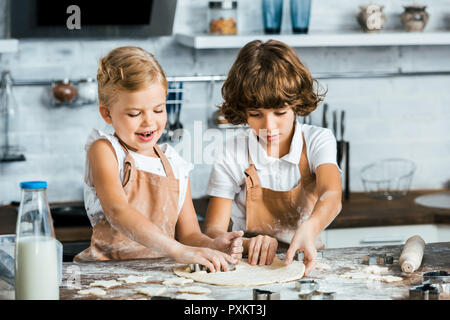Bezaubernd lächelnde Kinder in Schürzen Zubereitung Teig für leckere Cookies Stockfoto