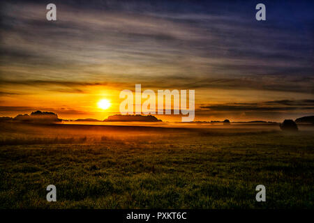 Nebeliger morgen im Dorf. Hellen schönen Sonnenaufgang. Bunte sunrise außerhalb. Fantastische nebligen Bereich mit frischem grünem Gras. Stockfoto