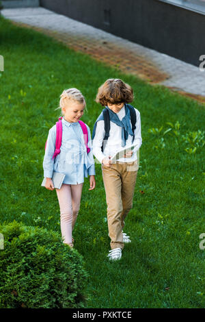 Hohe Betrachtungswinkel von schoolkids mit Rucksäcken Holding digital Tablet beim zusammen stehen auf grünen Rasen Stockfoto
