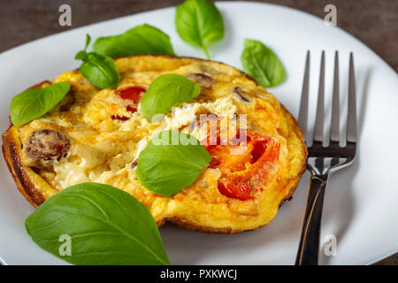 Frühstück essen - Omelette mit Würstchen, Käse, Zwiebeln und Tomaten auf dem weißen Teller Stockfoto