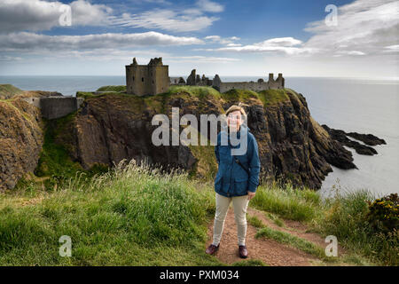 Schottische weiblichen touristische Besucher an der Spitze der Klippe über der alten Halle Bucht mit Donnottar Burgruine auf der Nordsee Schottland Großbritannien Stockfoto