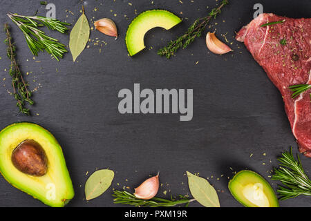 Frisches rohes Rindfleisch mit Avocado und Kräutern auf den schwarzen Stein Hintergrund Stockfoto