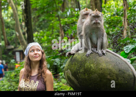Nahaufnahme: Junge kaukasier Frau für ein Foto mit niedlichen Affen auf der Schulter posieren. Neugierig macaque Ansätze reisenden Mädchen durch einen Sprung auf die Schulter. Stockfoto