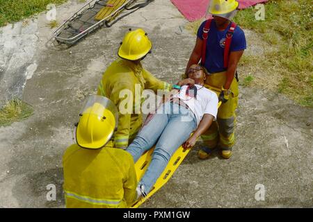 Feuerwehrleute aus dem Bridgetown Feuerwehr bewerten und einen freiwilligen Schauspieler während einer Messe Unfallversicherung bohren unterstützen auf dem Gelände der ehemaligen Glendairy Gefängnis. Das Szenario wurde auf der Idee, dass ein Erdbeben verursacht ein Hotel zum Einsturz und lokalen Notfalldienste und Barbados Defence Force (BDF) Personal zusammen zu retten und den Überlebenden zu behandeln. Tradewinds 2017 Regionale Beobachter und Assessment Team (ROAT) Mitglieder aus mehreren Ländern die Ausübung, um sich Notizen zu machen und eine Bewertung für Barbados Beamten erstellen beobachtet. Der Bericht wird Ideen von Weisen Notdienste enthalten Stockfoto