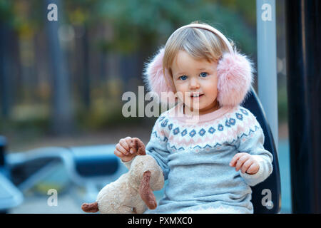 Portrait von süße Blondine kleines Mädchen in schönen, warmen Kleid und Winter Fellimitat gehörschützer am Spielplatz Stockfoto