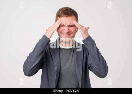 Studio Foto von gut aussehenden Kaukasier Mann zeigt, wie viel den Kopf schmerzt, Schmerzen, Elend und erschöpft Stockfoto