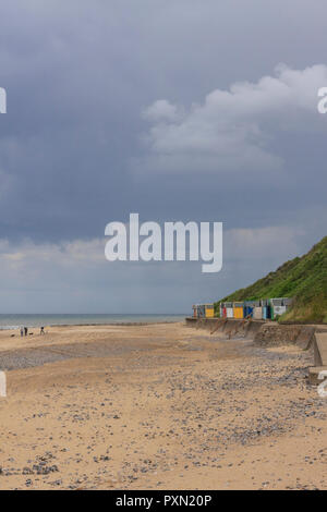 Bunten Badekabinen, Menschen am Strand mit Hunden, mit Gewitterwolken am Horizont. Cromer, Norfolk, England, Großbritannien Stockfoto