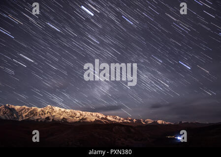 Bunte Titel der Sterne in der Form von Spuren in den Sternenhimmel vor dem Hintergrund der schneebedeckten Berge mit beleuchteten Mond Stockfoto