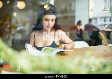 Portrait einer jungen schönen Mädchen allein in einem Cafe sitzen und Lesen einer Modezeitschrift. Stockfoto