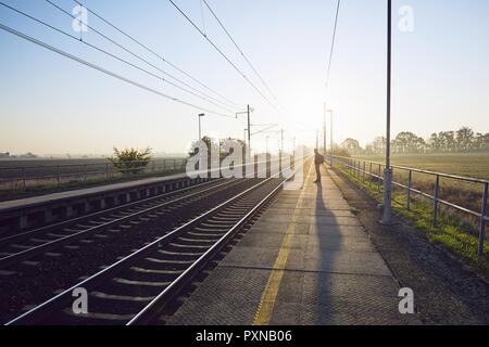 Allein junger Mann mit Rucksack warten auf Zug am Bahnhof bei Sonnenaufgang. Stockfoto