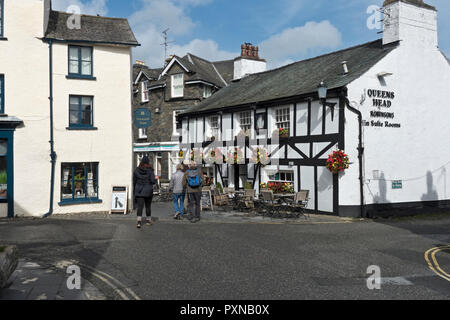 Menschen, die im Spätsommer am öffentlichen Pub des Dorfs Queens Head vorbeilaufen Hawkshead Cumbria England Großbritannien GB Großbritannien Stockfoto