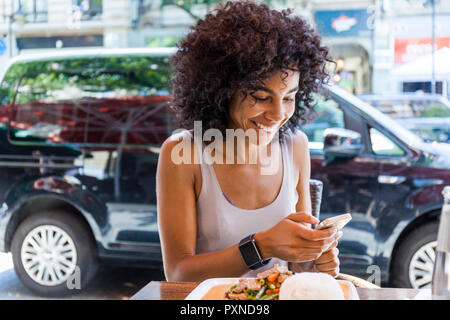 Portrait von lächelnden jungen Frau mit Sitzen im Bürgersteig Restaurant an der Zelle Telefon Stockfoto