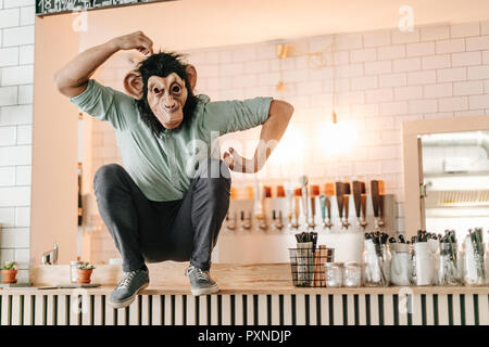 Mann, der Affe Maske, sitzen auf den Zähler einer Bar, kratzen Kopf Stockfoto