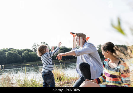 Glückliche Familie entspannen am Flußufer, Vater und Sohn spielen mit Spielzeug Flugzeug Stockfoto