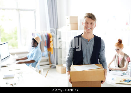 Portrait der junge lächelnde Mann, online zu bestellen und stehen im Atelier mit anderen Designern im Hintergrund arbeiten Stockfoto