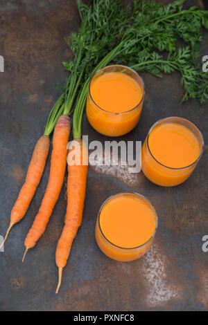 Drei Gläser frischen Karottensaft und drei Karotten Stockfoto