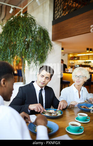 Die Gruppe von Kollegen ein business talk beim Mittagessen im Restaurant, Sie sitzen und essen Salat und Kaffee trinken Stockfoto