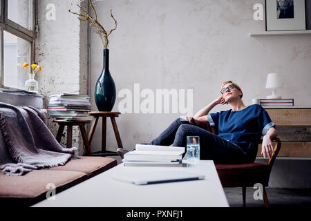 Nachdenkliche Frau sitzt auf einem Sessel im Loft suchen Stockfoto