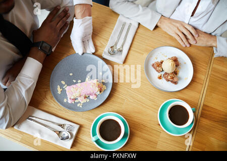 Close-up Tisch mit Teller und Tassen Kaffee und Business Leute am Tisch sitzen beim Business Lunch im Restaurant Stockfoto
