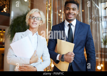 Porträt der jungen afrikanischen Geschäftsmann in Anzug und Reife lächelnd Geschäftsfrau mit Ordner im modernen Restaurant Stockfoto