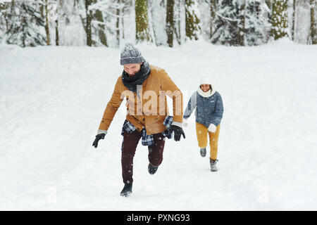 Gerne Begeistert junge Freunde in geschwollene Jacken im Winter Wald läuft beim spielen Tag im Urlaub Stockfoto