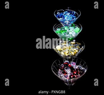 Bunte Perlen in einer Linie der Martini Gläser vor einem schwarzen Hintergrund. Gläser Leuchten von oben. Stockfoto