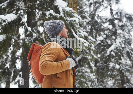 Inhalt inspiriert hübscher junger Mann in warme Mütze und Schal alleine unterwegs und der Betrachtung Wald um im Winter Stockfoto