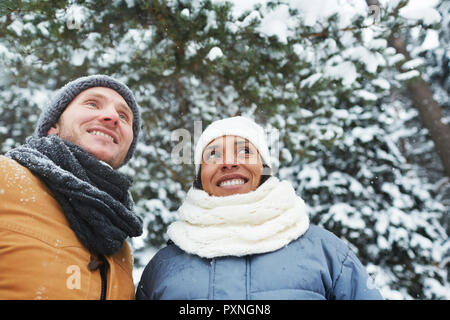 Lächelnd positive junge multi-ethnischen Paar in warmen Mützen und Schal um und genießen die Schönheit der Natur beim Wandern im Winter Park und sein Stockfoto