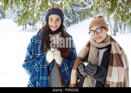 Porträt von zwei glückliche junge Frauen im Winter Resort posing Holding Tassen mit heißem Kakao und freundlich lächelnd an Kamera suchen Stockfoto