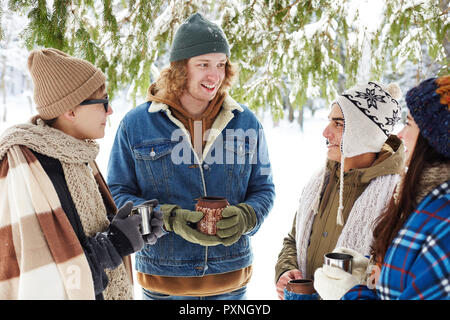 Gruppe von Jugendlichen trinken heißen Kakao im Winter Wald und Plaudern und Genießen Sie die Zeit im Resort Stockfoto