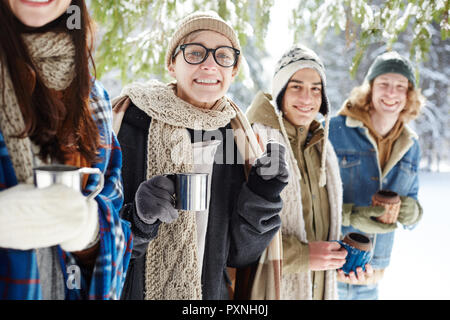 Gruppe von Jugendlichen fröhlich in die Kamera lächeln, während im Winter Wald in der Zeile posiert, Fokus auf junge Frau mit Metall Schale Stockfoto
