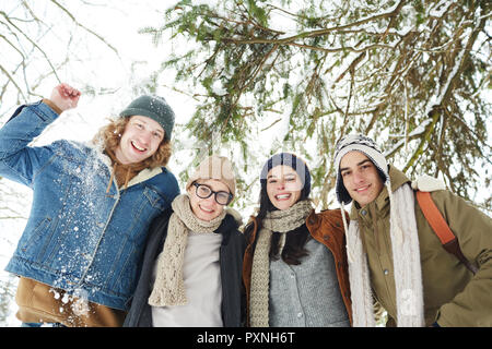 Low Angle Porträt der Gruppe der glückliche junge Menschen im Winter Resort unter dem Tannenbaum im wunderschönen verschneiten Wald posing und lächelnd an Kamera Stockfoto
