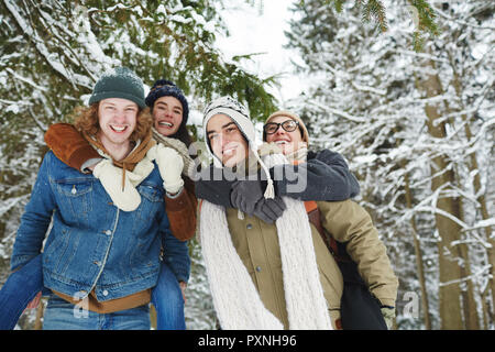 Porträt von zwei schöne junge Paare Spaß auf Winter Resort und in die Kamera lächeln, während piggyback spielen in den verschneiten Wald, kopieren Raum Stockfoto