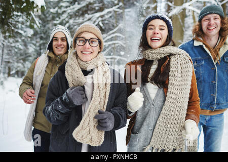 Taille bis Portrait von vier unbeschwerte junge Menschen in Richtung Kamera, während Spaß im Winter Wald während der Ferien Stockfoto