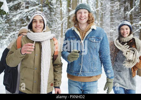 Taille bis Portrait von vier unbeschwerte junge Menschen in Richtung Kamera läuft, während Spaß im Winter Wald während der Ferien, konzentrieren sich auf zwei lächelnde Männer in Stockfoto