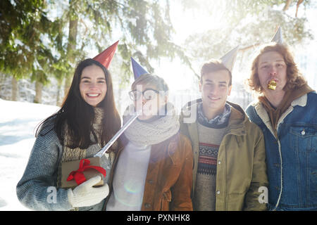 Gruppe von vier jungen Menschen feiern Weihnachten draußen im schönen Wald, alle tragen Partei Kappen Stockfoto