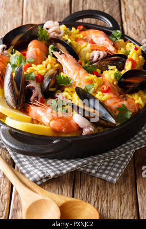 Spanische Paella mit Shrimps, Muscheln, Fische und Tintenfische close-up in einer Pfanne auf dem Tisch. Vertikale Stockfoto