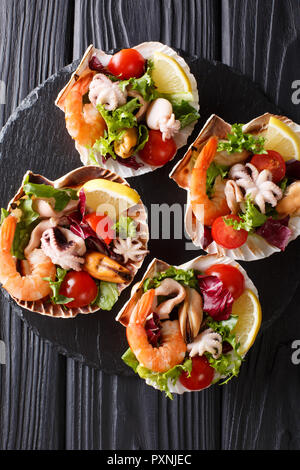 Frische Meeresfrüchte Salat mit Gemüse und Zitrone serviert im Seashells close-up auf den Tisch. Vertikal oben Ansicht von oben Stockfoto