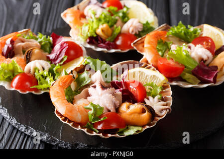 Leckeren Salat aus gekochtem Fisch und Meeresfrüchte Garnelen, Tintenfische, Muscheln, Tintenfisch und Jakobsmuscheln mit Gemüse in seashells Close-up auf dem Tisch. Horizontale Stockfoto