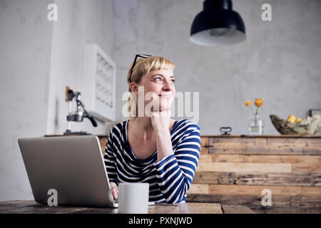Porträt der lächelnde Frau mit Laptop und Kaffeebecher sitzen Stockfoto