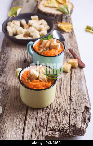 Herbst Kürbis Suppe auf hölzernen Tisch in ländlichen Tassen serviert, gesunde, vegetarische Mahlzeiten Stockfoto