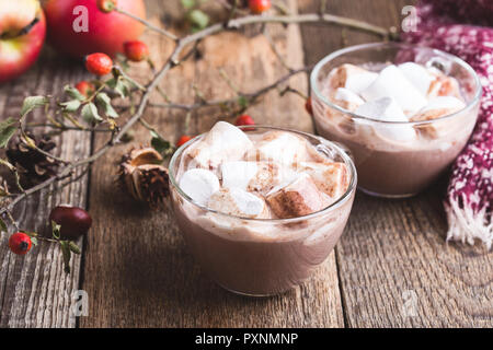 Schaumige heiße Schokolade im Glas Becher mit Marshmallows auf rustikalen Holztisch Stockfoto