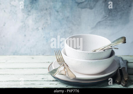 Stapel von sauberen Teller mit Besteck auf der Oberseite über Holz- Tabelle. Pastelltöne. Stockfoto