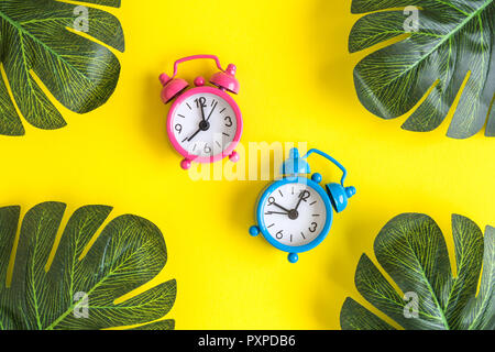 Kleine Wecker und tropischen Palmen Blätter auf gelben Hintergrund. Sommer minimal kreatives Konzept. Stockfoto