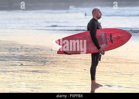 Surfen UK - eine ausgereifte Surfer auf den Fistral Beach mit einem Schwanz Surfboard schlucken. Stockfoto